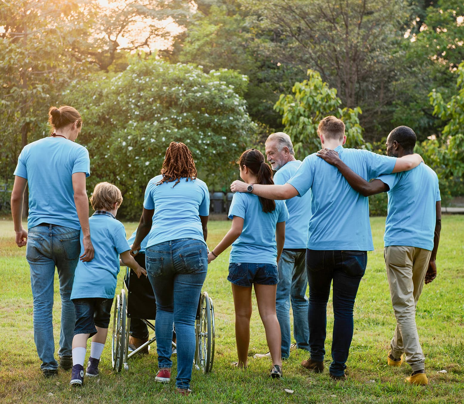 Åtte personer går sammen i grønt landskap, én i rullestol. Alle har lyseblå skjorter.